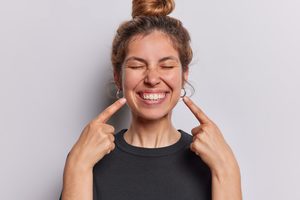 Woman squinting eyes smiling broadly pointing to her teeth